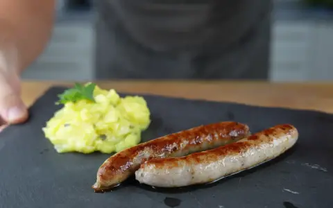 Zwei goldbraune Bratwürste mit Kartoffelsalat, perfekt für alle, die Bratwurst selber machen wollen.