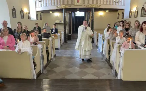 Uroczyste odnowienie przyrzeczeń chrzcielnych w kościele. Dzieci z zapalonymi świecami siedzą w ławkach, a ksiądz błogosławi zgromadzonych.