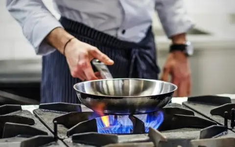 Chef calienta sartén de acero inoxidable para cocinar sobre llama azul de gas.