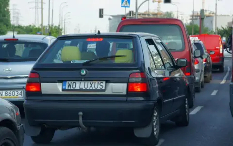 Czarny samochód z indywidualnymi tablicami rejestracyjnymi "WO LUXUS" w korku ulicznym.