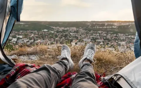 Nogi w butach sportowych na tle malowniczego krajobrazu z miasteczkiem. Wspaniały widok z namiotu podczas **camping portugalia**.
