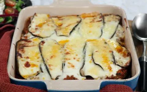 En ugnsform med en gyllene, bubblande moussaka, redo att serveras. Perfekt för ett mysigt middagsrecept.