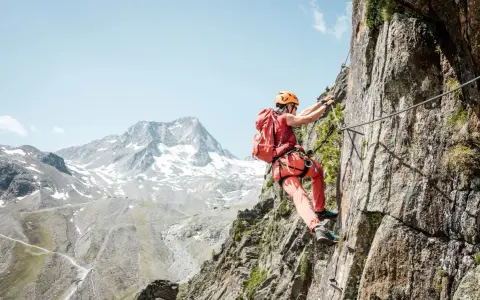 Wspinaczka po skalnej ścianie na via ferrata w Niemczech. Widok na ośnieżone góry w tle.