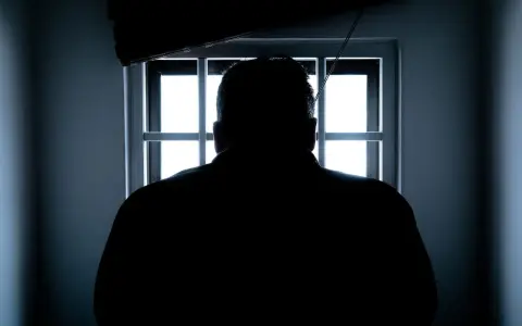 Sylwetka mężczyzny wpatrująca się w okratowane okno. Czekam na dzień, gdy dozór policyjny kiedy się kończy i zobaczę wolność.