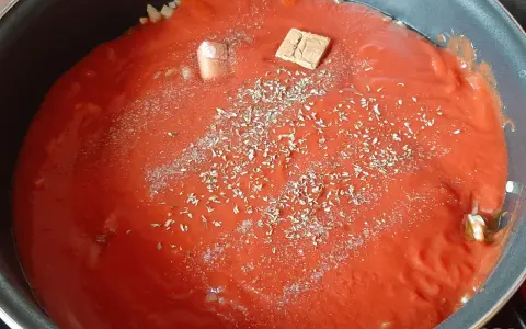 Préparation d'une recette de sauce tomate maison avec des herbes et un cube de bouillon dans une poêle.