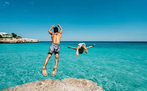 Due ragazzi si tuffano in un mare cristallino, un'idea perfetta per chi cerca dove andare in vacanza con pochi soldi in Italia.