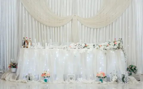 Elegancka ścianka za parą młodą inspiracje: białe zasłony, kwiaty, napisy "Wedding", "Love", "Mrs & Mr".