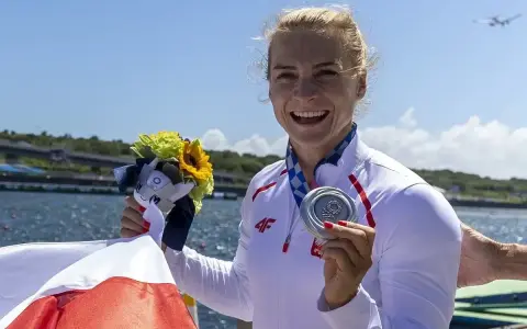 Uśmiechnięta sportsmenka z medalem i bukietem kwiatów, symbol sukcesu najlepszych polskich kajakarzy.