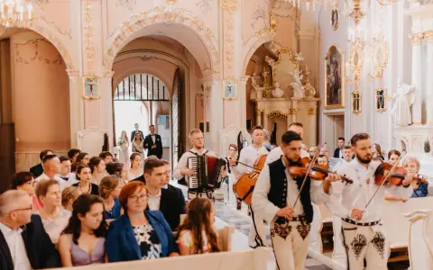 Muzycy w strojach ludowych zapewniają oprawę muzyczną ślubu w kościele. Grają na skrzypcach i akordeonie.