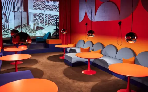 En färgstark lounge med soffor, orange bord och en projektion av Nanna Ditzels design.