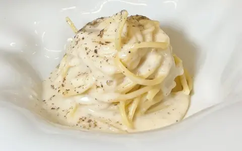 Un piatto di spaghetti cremosi, conditi con un'abbondante dose di cacio e pepe, cosparsi di pepe nero macinato.