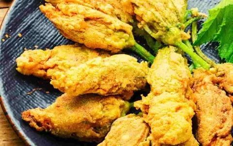 Fiori di zucca ripieni dorati e croccanti, serviti su un piatto blu scuro.