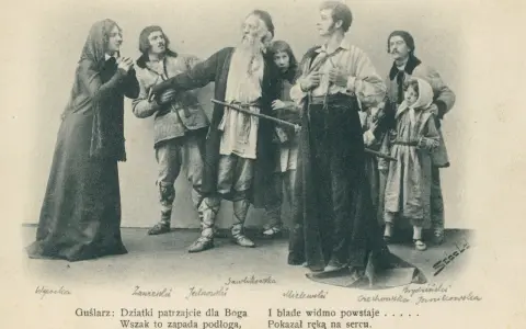 Grupa postaci w strojach ludowych, w tym starszy mężczyzna z brodą, młodzi ludzie i dzieci.