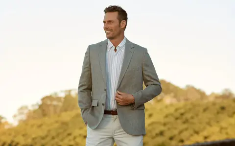 A man in a light grey blazer, striped shirt, and beige pants. This is a stylish option for what to wear to an engagement party.