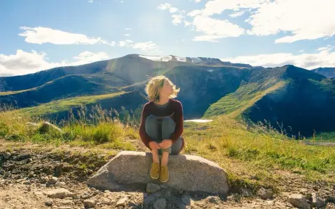 Ragazza seduta su una roccia, con i capelli mossi dal vento, ammira il panorama montano. Un momento di pace mentre camminare nella natura.