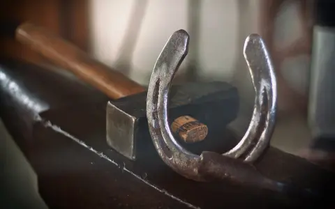 Un fer à cheval usé repose sur une enclume, à côté d'un marteau. L'artisanat du maréchal-ferrant est palpable.