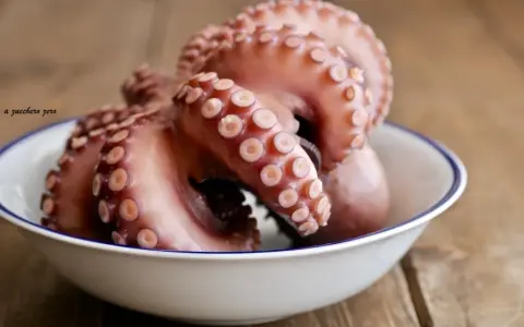 Pulpo listo para cocer en un cuenco blanco con borde azul, sobre una mesa de madera rústica.