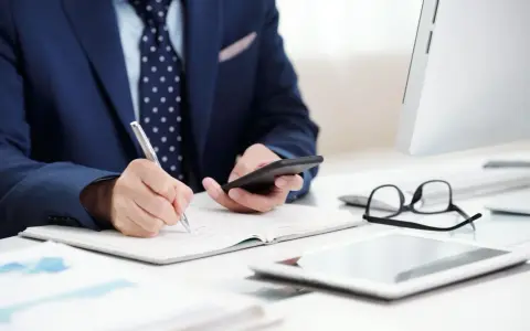 Biznesmen notuje, analizując dane. Rozważa przedawnienie kosztów komorniczych, trzymając telefon.