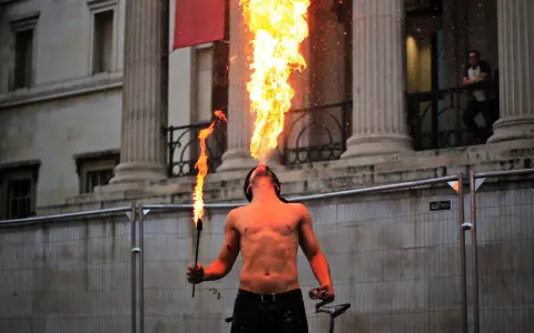 Feuerspucker bläst eine Flamme, während er eine Fackel hält. Der Mann brennt Vodka und zeigt seine Kunst vor einer beeindruckenden Säulenarchitektur.