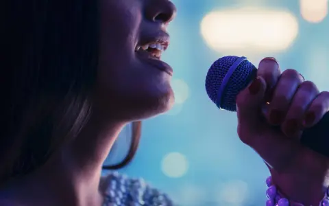 Kobieta śpiewa do mikrofonu. Czy to playback? Wokalistka z błyszczącą suknią i fioletowym mikrofonem.