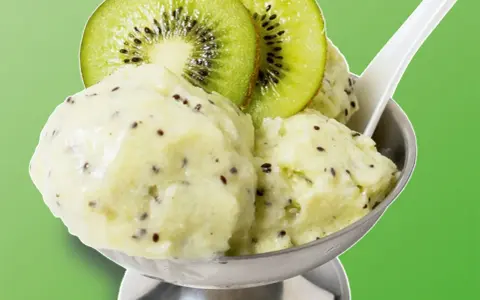 Erfrischendes Kiwi-Eis in einer Schale, garniert mit frischen Kiwischeiben. Ein Löffel steckt darin, bereit zum Genuss.
