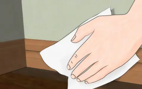 Mano limpiando rodapiés de pintura con un paño blanco.