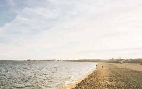 Spokojny dzień nad morzem na Kaszubach. Pusta plaża, delikatne fale i kilka osób spacerujących brzegiem.