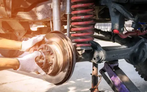 Ręce w białych rękawiczkach montują tarczę hamulcową w wielowahaczowym zawieszeniu samochodu.