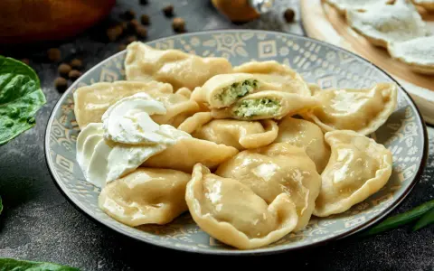 Talerz pierogów ze szpinakiem i twarogiem, z kleksem śmietany.