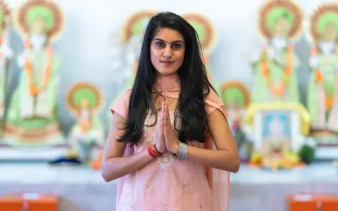 En ung kvinna i traditionella kläder med händerna i bön framför hinduiska statyer, en bild som väcker tankar om mantra hinduism.