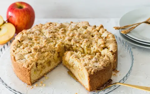 Ein saftiger Apfelkuchen mit Streuseln, ein Stück herausgeschnitten, daneben Äpfel.