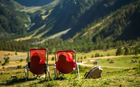 Dwie osoby w czerwonych leżakach podziwiają widok na Alpy w Austrii. Idealne miejsce na camping.