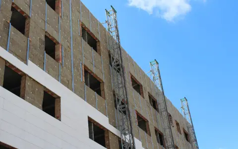 Fachada de edificio en construcción, con aislamiento térmico y andamios. Un plan rehabilita la estructura para mejorar su eficiencia energética.