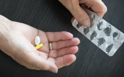 Dłoń trzyma białą i żółtą tabletkę, obok pusty blister. Może to być cytrynian magnezu.
