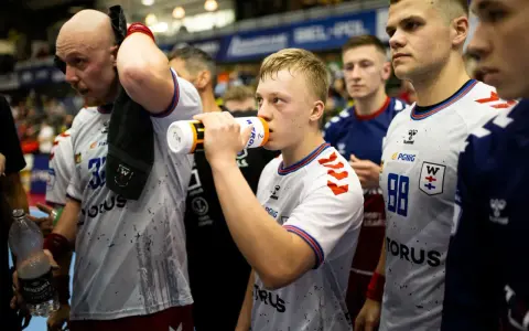 Szymon Adamczyk pije wodę z bidonu, otoczony kolegami z drużyny.