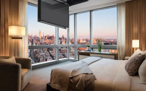 Camera da letto con vista su New York, dove una tv nascosta a soffitto scompare quando non serve, lasciando spazio al panorama.