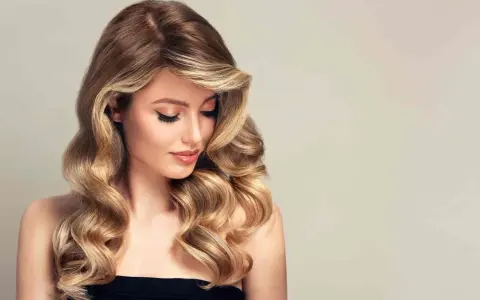 Kobieta z falowanymi, brązowo-blond włosami, delikatnym makijażem i spojrzeniem skierowanym w dół.