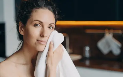 Une femme se sèche le visage avec une serviette. Elle a une peau radieuse, peut-être grâce aux 10 aliments bon pour la peau.