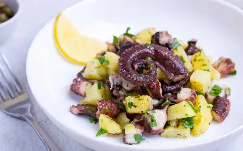 Ensalada de pulpo y patatas, un ejemplo de recetas sanas con pulpo. Servida en plato blanco con limón y perejil.