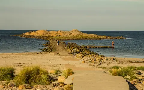 En stenpir leder ut till en klippö. En person går på piren, en annan badar. Perfekt för aktiviteter i Halmstad.