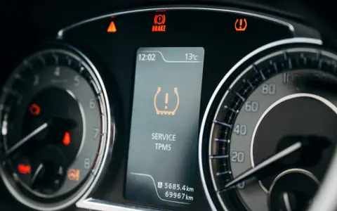 Na desce rozdzielczej świeci się kontrolka niskiego ciśnienia w oponach (TPMS). Obok widać wskaźnik hamulca i ostrzeżenie o temperaturze.