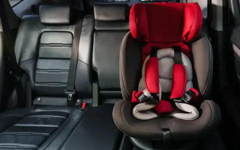 Czerwony fotelik dziecięcy z pasami bezpieczeństwa zamontowany w samochodzie. System isofix w samochodzie zapewnia bezpieczne podróżowanie najmłodszych.