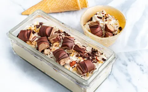 Lody Kinder Bueno w pojemniku i wafelku, posypane orzechami i czekoladą.