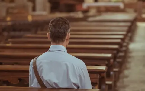 Mężczyzna siedzi w pustej ławce kościelnej, pogrążony w zadumie. To chwila wyciszenia i duchowości.