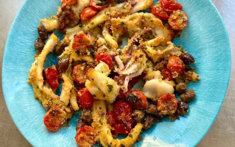 Calamari gratinati al forno su piatto blu, con pomodorini e olive.