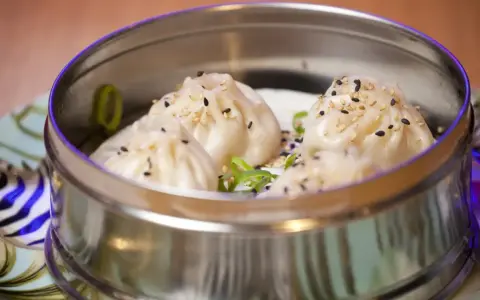 Deliciosos dumplings al vapor, cubiertos con semillas de sésamo y cebolleta, servidos en una vaporera metálica.