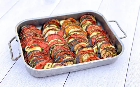 Un plat de tian de légumes, prêt à cuire, avec des rondelles de courgettes, aubergines et tomates joliment disposées. Parfait pour faire un tian de légumes la veille.