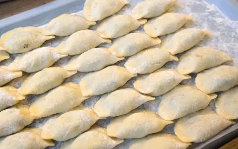 Ułożone na tacy surowe pierogi, posypane mąką.