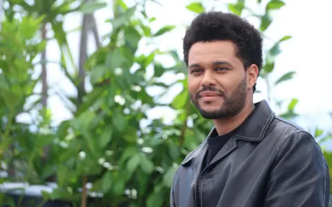 The Weeknd trägt eine schwarze Lederjacke vor einem grünen, unscharfen Hintergrund.