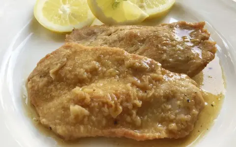 Deliziose scaloppine al limone, succulente e dorate, servite con spicchi di limone fresco.